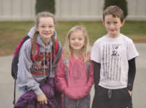 Three children smile in front of the Haines school
